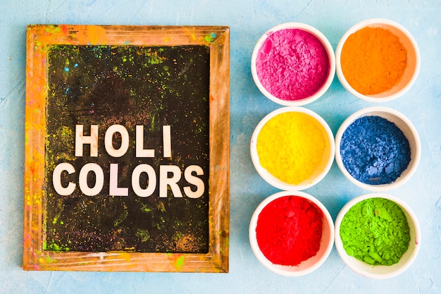 Color powder in the white bowls near the wooden slate with holi color text