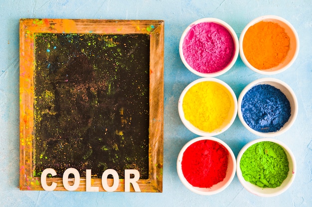 Color text on wooden slate with holi color powder in the white bowls