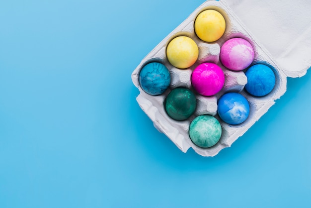 Colored eggs in carton rack on blue background 