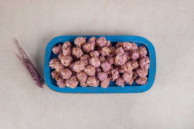 Free Photo colored stalk of wheat next to a wooden platter of candied popcorn on marble.