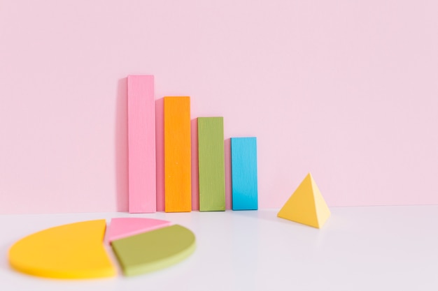 Free Photo colorful bar graph; pie chart and yellow pyramid on desk over pink background