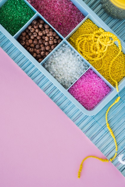 Colorful beads in blue case on placemat over the pink background