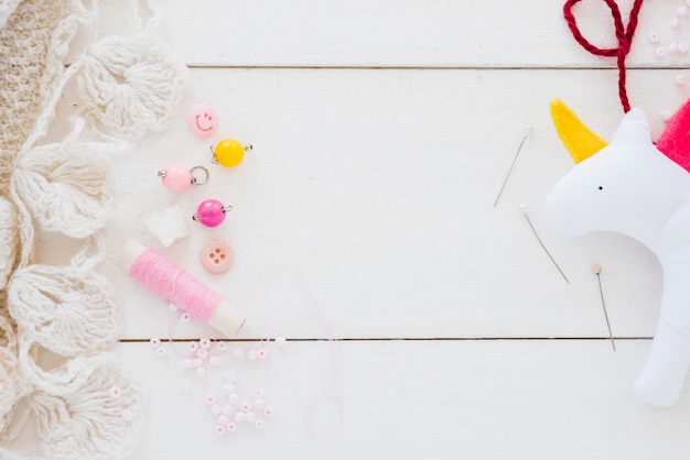 Free Photo colorful beads; spool; needle and rag unicorn on white wooden desk