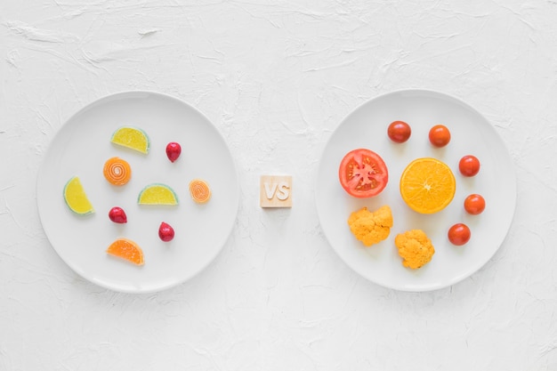 Free photo colorful candies versus fresh vegetables on white plate over background