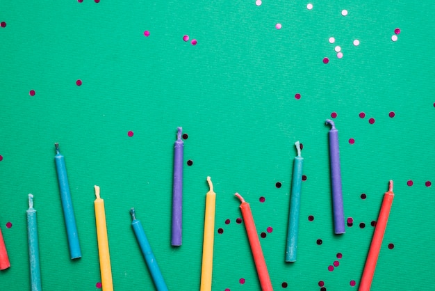 Colorful candles with confetti on green background