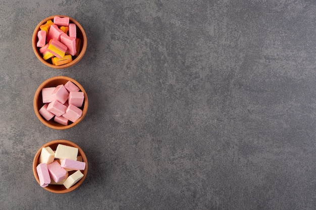 Colorful chewing gums placed in clay bowls on a stone table .