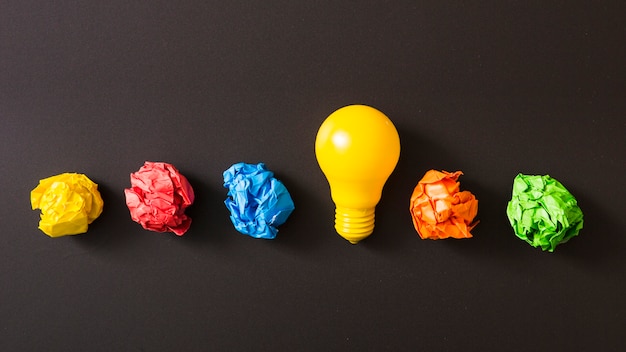 Free photo colorful crumpled paper ball with yellow light bulb against black background