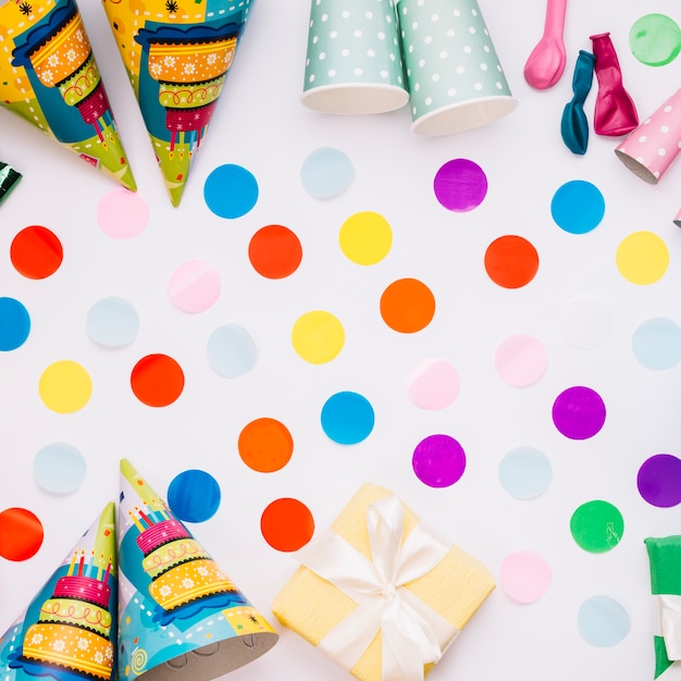 Free photo colorful decorated confetti with party hats; gift box; balloons and wrapped gift box on white background