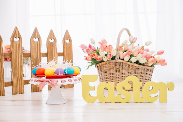 Colorful easter eggs; tulips basket with yellow easter text on wooden desk