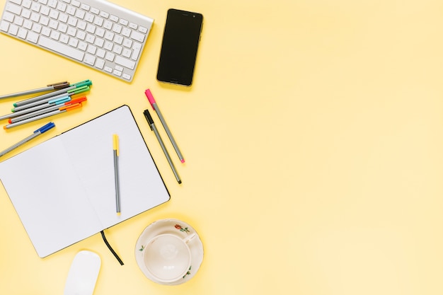 Colorful felt-tip pens; notebook with keyboard and cellphone on yellow background