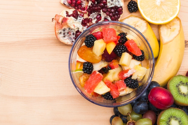 Free photo colorful fruit salad in glass bowl on wooden desk