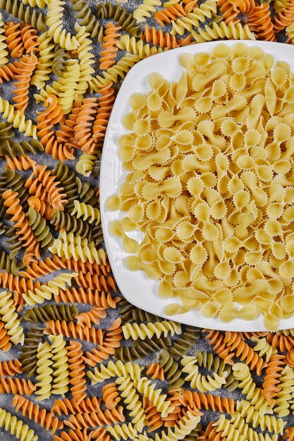 Colorful fusilli and bowl of raw pasta on marble table.