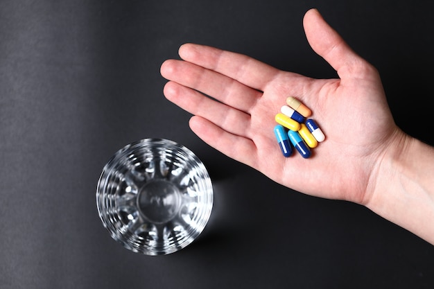 Free Photo colorful medical pills in the hand of a person and a glass of water. top view.