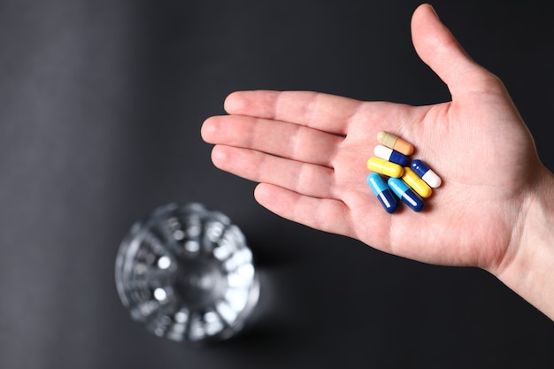 Free Photo colorful medical pills in the hand of a person and a glass of water