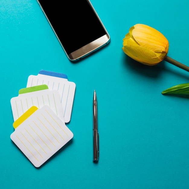 Colorful notepads with pen; cell phone and yellow tulips on blue background