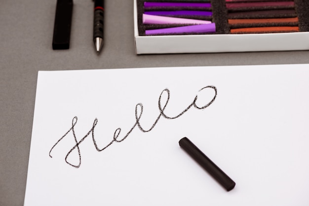 Free photo colorful pastel, pen, paper with word hello on grey table