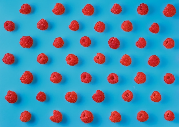 Free photo colorful pattern of ripe raspberry berries on a bright blue background. top view, berry background