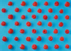 Free photo colorful pattern of ripe raspberry berries on a bright blue background. top view, berry background