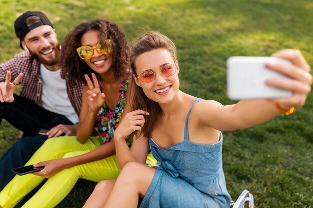 Colorful stylish happy young company of friends sitting park, man and women having fun together