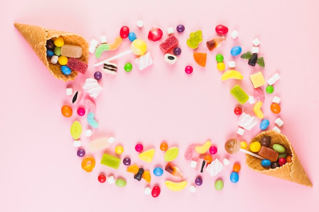 Colorful sweet candies with two ice cream waffle cone on pink surface