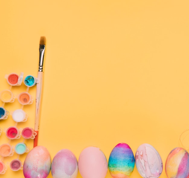 Free photo colorful watercolor paint with paintbrush and easter eggs on yellow background with space for writing the text