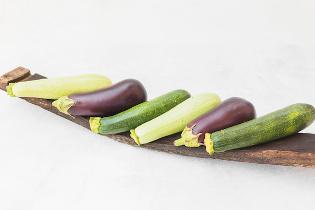 Colorful whole harvested eggplants on wooden tray against white background