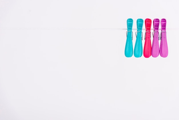 Colourful clothes-pins hanging on white clothesline