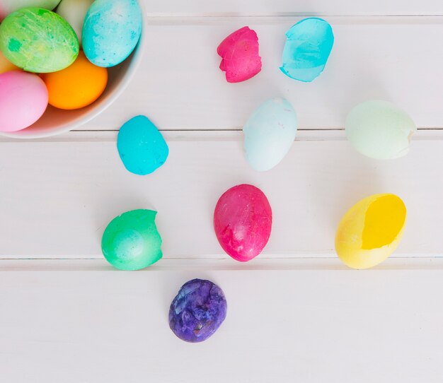 Colourful Easter eggs in bowl near shell on desk