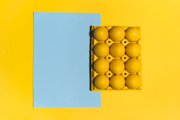 Colourful Easter eggs in rack with blank paper sheet on table