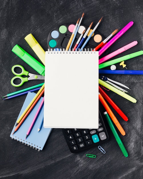 Free photo colourful stationery, paints, calculator under notebook on grey background