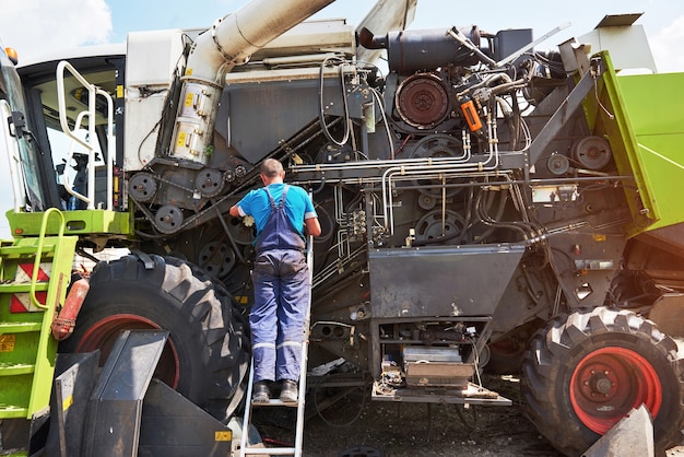 Combine machine service, mechanic repairing motor outdoors.