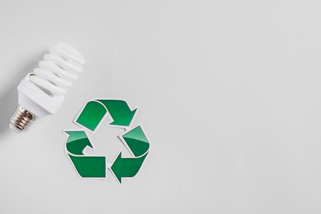 Compact fluorescent light bulb and recycle icon on white backdrop