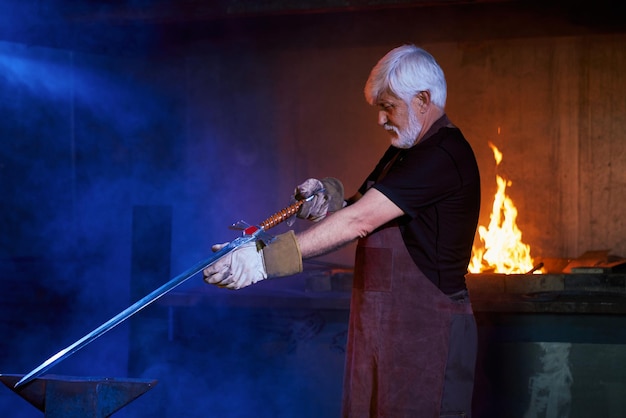 Free photo competent aged blacksmith making sword at forge