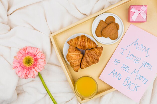 Composition of bakery, glass and paper with words on tray near flower