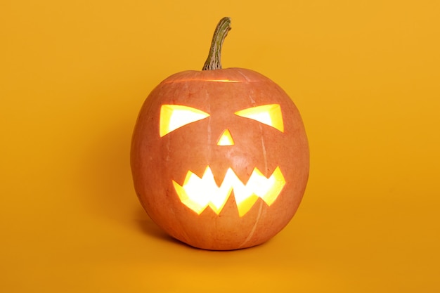 Composition of glowing light from inside jack o lantern, pumpkin isoalted on yellow, celebrating holiday, last October night, orange pumpkin on studio wall. Halloween concept.