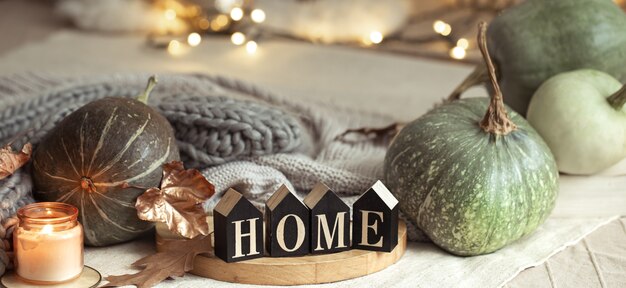 Composition homely autumn atmosphere in the interior with pumpkins and wooden letters with the words home on blurred background with bokeh. Close up.