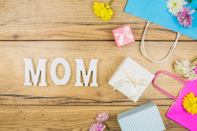 Composition of mom title near fresh flowers, present boxes and paper packets