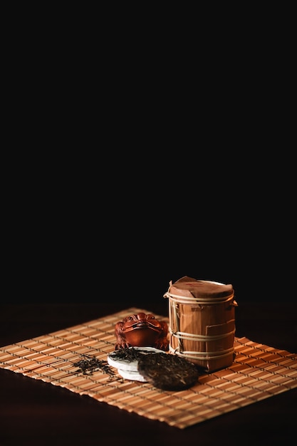 The composition of puer tea with golden toad on a bamboo mat. Black background.