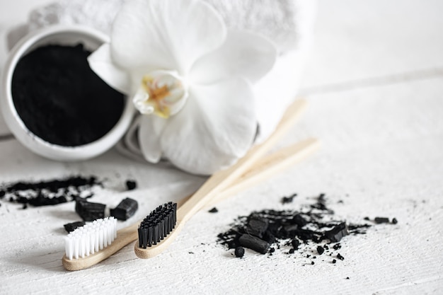 Composition with a wooden natural toothbrushes, black teeth whitening powder and orchid flower copy space.