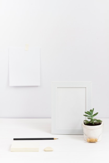 Free photo composition of workplace with white frame and plant vase