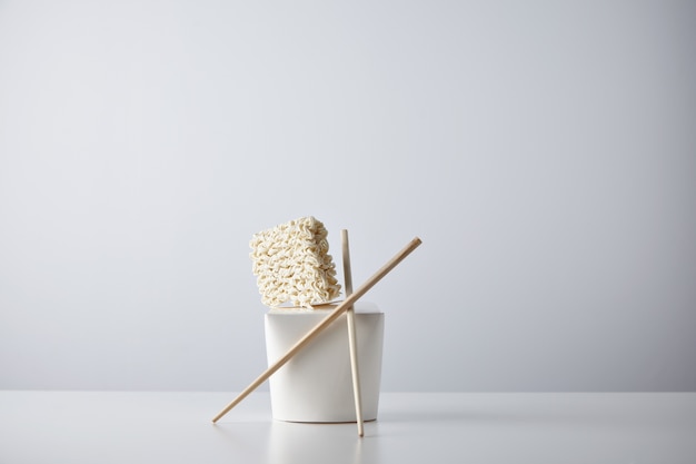 Free photo compressed dry noodles brick presented on top of blank takeaway box with chopsticks isolated on white in center