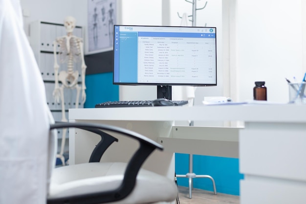 Free photo computer with medical patient files on screen standing on table in empty doctors office during medical examination. hospital office equipped with professional modern furniture. health care support