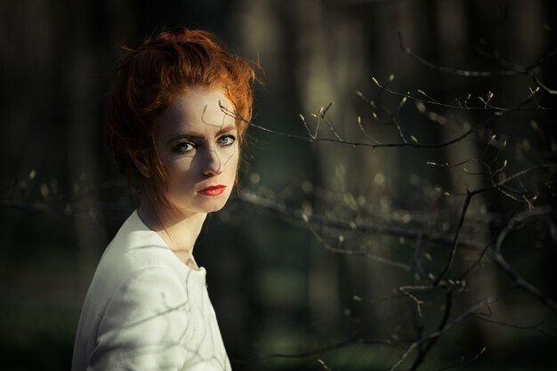 Conceived redheaded girl with red lips looking into the frame