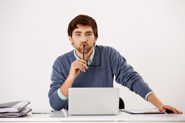 Concentrated businessman sitting at the office desk using laptop looking