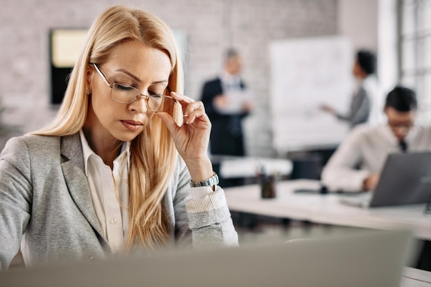 Free Photo concentrated businesswoman working at her desk in the office there are people in the background