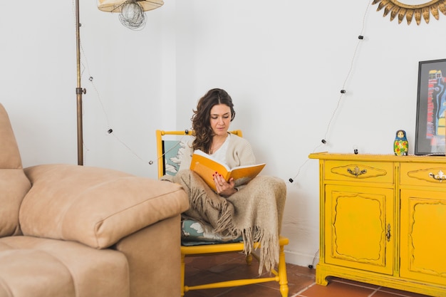 Free Photo concentrated girl reading a book sitting on a yellow chair