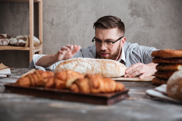 Concentrated man baker standing at bakery near bread.