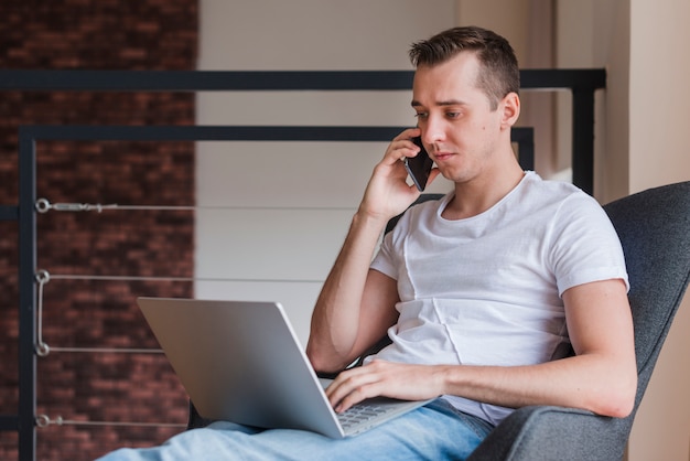 Concentrated man talking on smartphone and sitting on chair with laptop