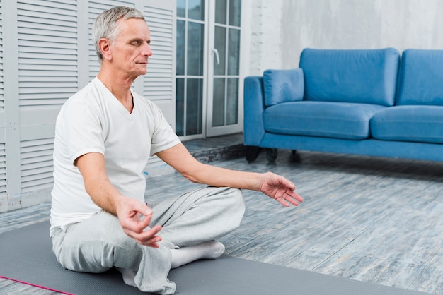 Free photo concentrated old man meditating on mat at home