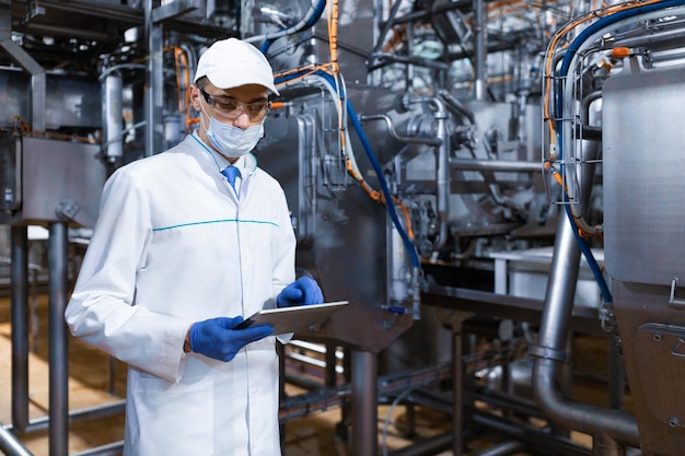 Concentrated technologist taking necessary notes with help of digital tablet while standing at production department of dairy factory inspector carries out control at the cheese factory